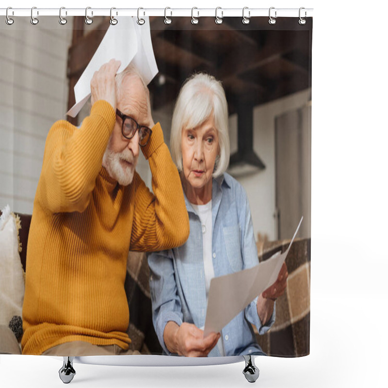 Personality  Disappointed Senior Husband Holding Bills Near Head Sitting Near Wife On Couch On Blurred Background At Home Shower Curtains