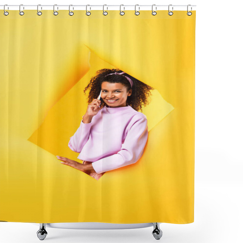 Personality  Cheerful African American Woman Talking On Smartphone And Looking At Camera Through Ripped Paper On Yellow Shower Curtains