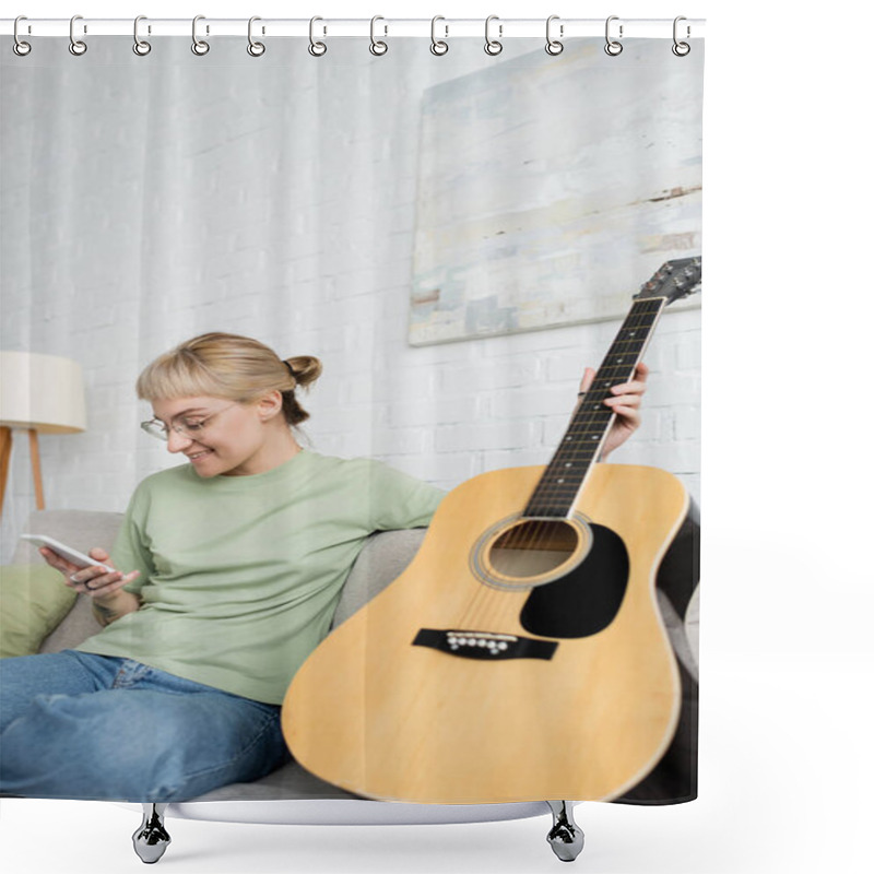 Personality  Happy Young Woman With Blonde And Short Hair, Bangs And Eyeglasses Using Smartphone While Sitting On Comfortable Couch Near Guitar In Modern Living Room With Painting On Wall  Shower Curtains