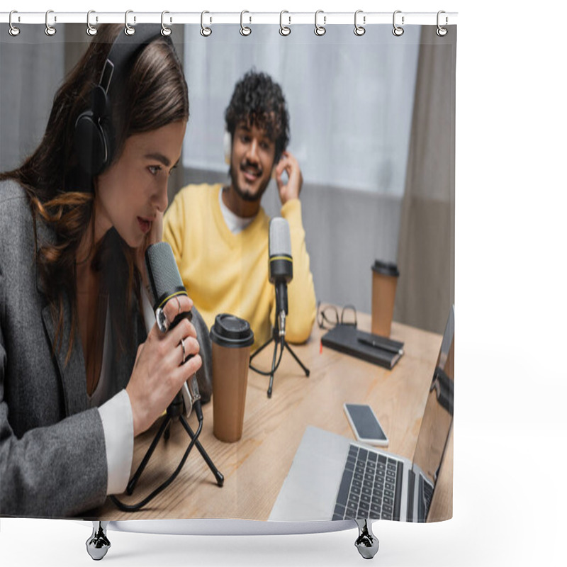 Personality  Brunette Radio Host In Headphones Talking In Professional Microphone Near Laptop, Smartphone With Blank Screen, Paper Cups, Notebook And Indian Colleague Smiling In Studio On Blurred Background Shower Curtains