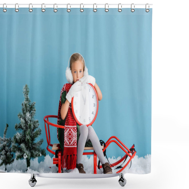 Personality  girl in winter earmuffs and scarf sitting in sleigh and holding clock near pines on blue shower curtains