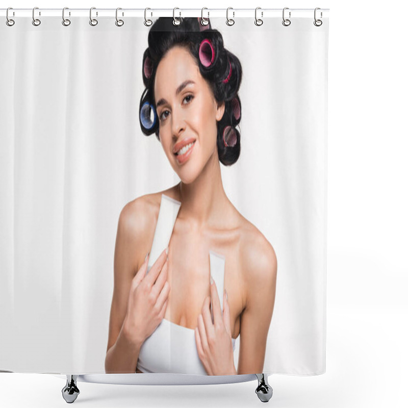 Personality  smiling young woman with curlers on head holding cream tubes near breast isolated on white shower curtains