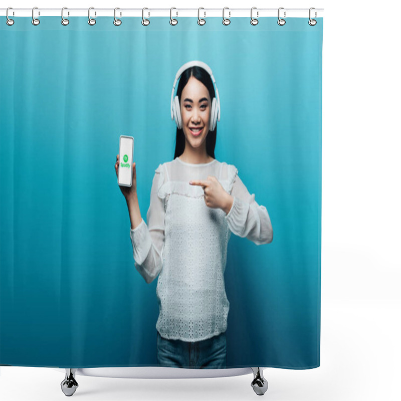 Personality  KYIV, UKRAINE - JULY 15, 2019: Smiling Asian Woman With Headphones Pointing With Finger At Smartphone With Spotify Logo On Blue Background Shower Curtains