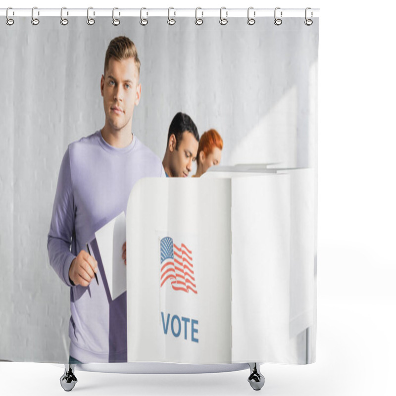 Personality  Man Looking At Camera While Holding Ballot Near Polling Booth With American Flag And Vote Lettering On Blurred Background Shower Curtains