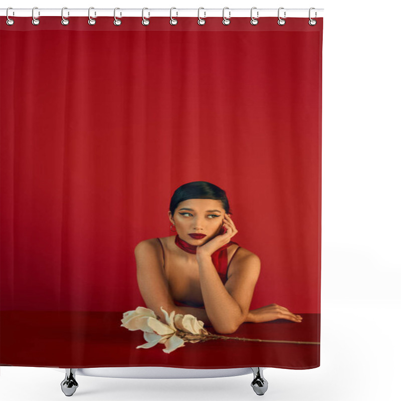 Personality  Pensive Asian Woman In Stylish Neckerchief, With Brunette Hair And Bold Makeup Sitting At Table Near While Orchid, Holding Hand Near Face And Looking Away On Red Background, Trendy Spring Concept Shower Curtains