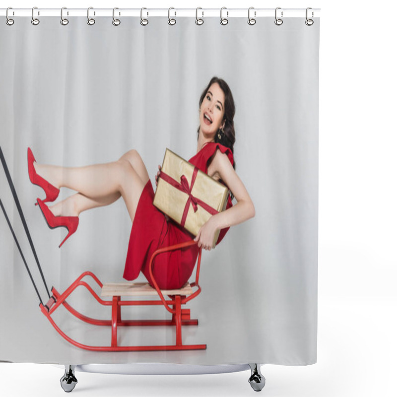 Personality  Cheerful Woman In Red Dress And Heels Holding Present While Sitting On Sleigh On Grey Background Shower Curtains