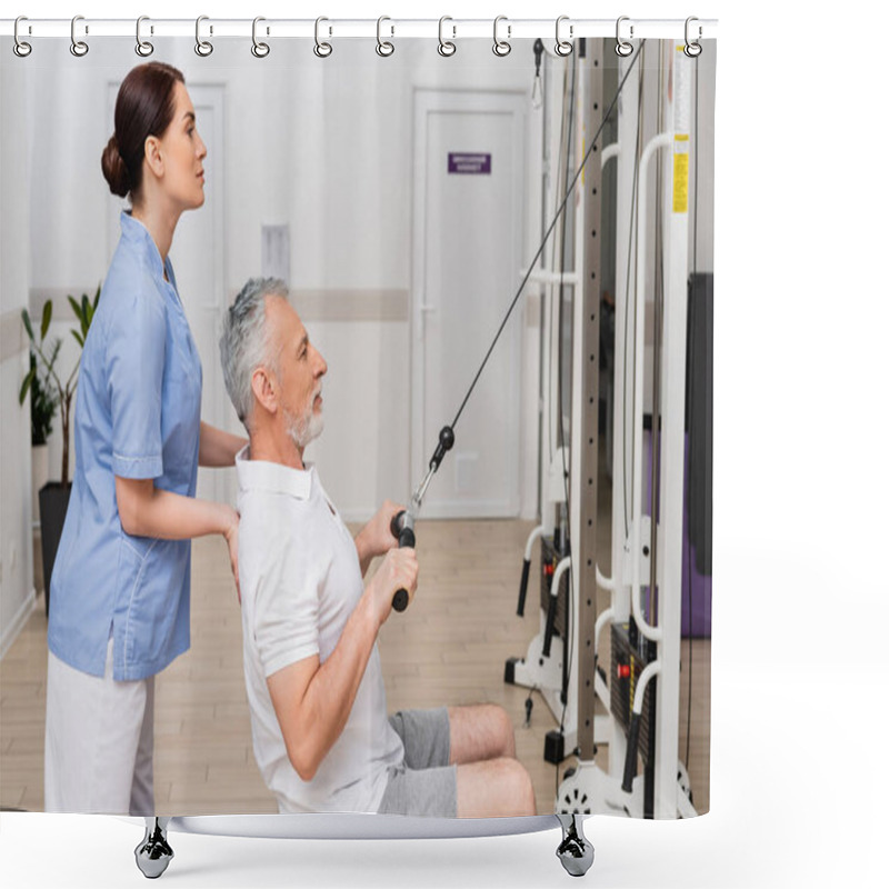 Personality  Side View Of Rehabilitologist Supporting Mature Man Exercising On Pull Cable Machine Shower Curtains