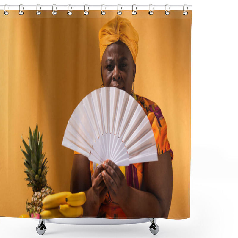 Personality  Serious Middle Aged African American Woman Sitting Near Fruits And Holding Fan On Orange Shower Curtains