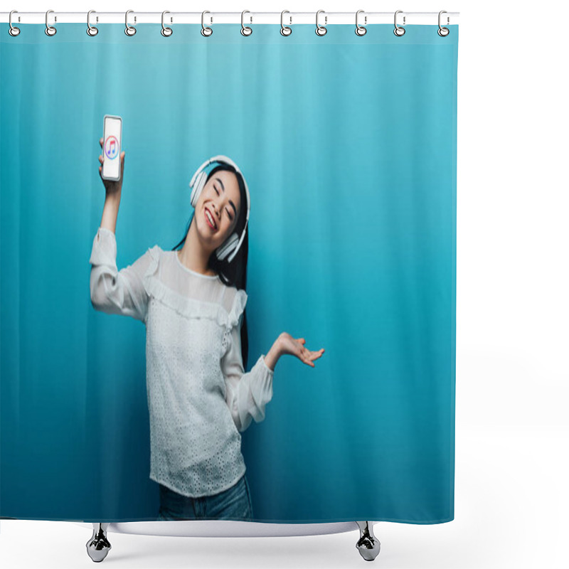 Personality  KYIV, UKRAINE - JULY 15, 2019: Smiling Asian Woman With Closed Eyes In Headphones Holding Smartphone With ITunes App And Dancing On Blue Background Shower Curtains