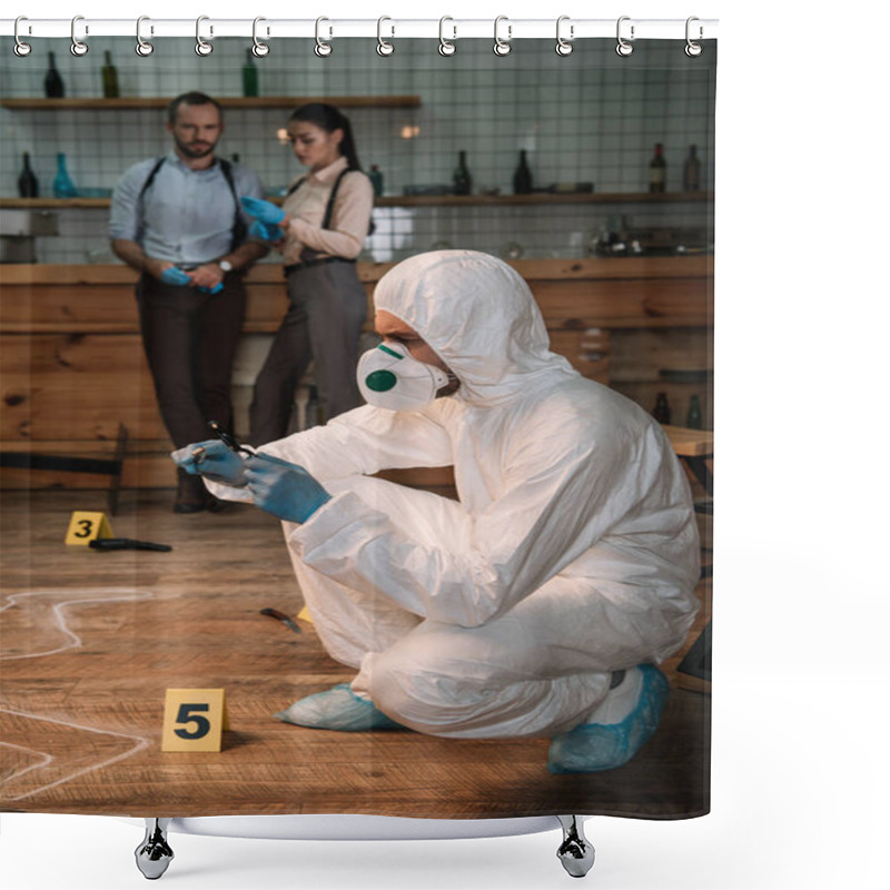 Personality  Concentarted Forensic Investigator Examining Evidence With Magnifying Glass At Crime Scene With Colleagues Working Behind Shower Curtains