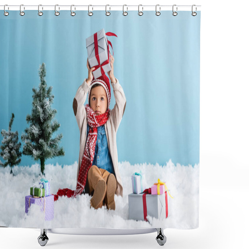 Personality  Boy In Hat And Winter Outfit Sitting On Snow And Holding Present Above Head Near Christmas Trees Isolated On Blue Shower Curtains